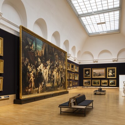Großer Museumsraum mit dunklen Wänden, historischen Gemälden, Sitzbänken und Oberlicht